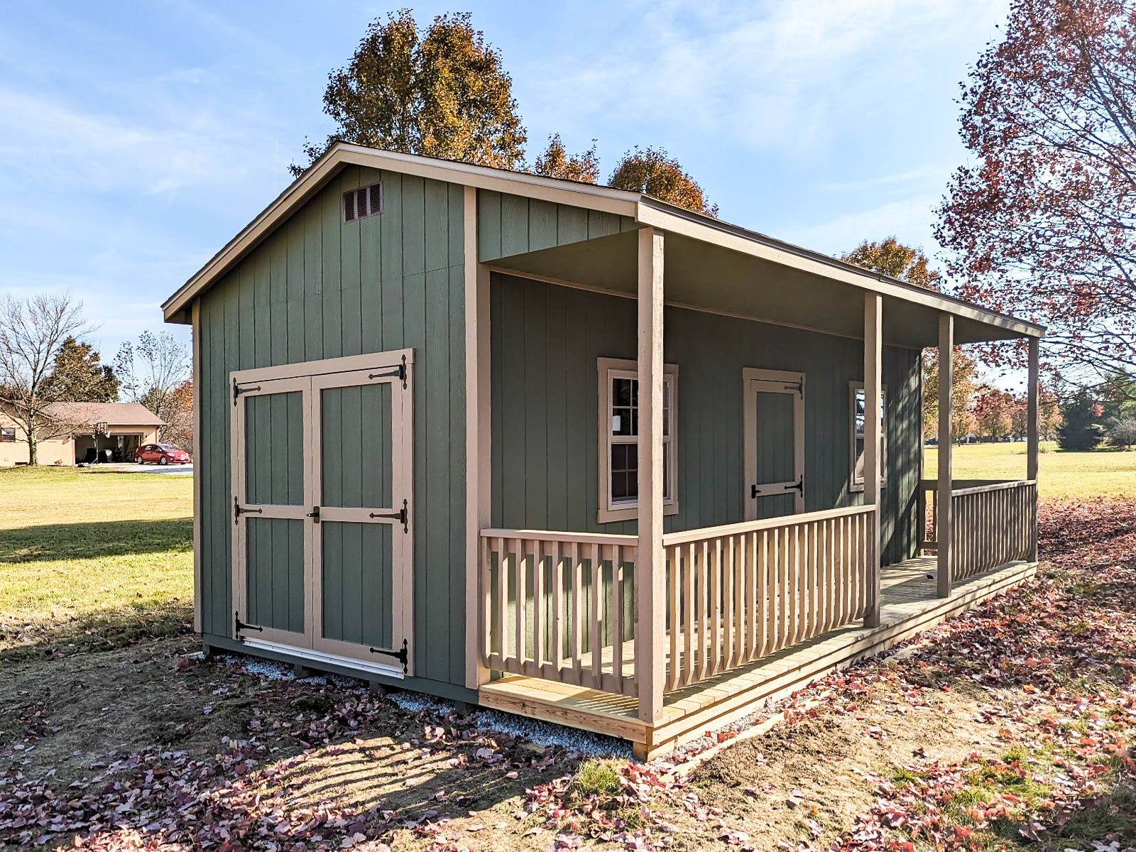 A green shed with a beige trim and a small porch area, featuring double doors on one side and a window. Depending on your location, you may or may not need a shed permit in Ohio.