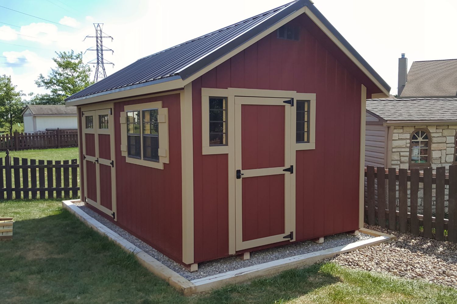Red Cape Cod shed with tan trim and black metal roof.