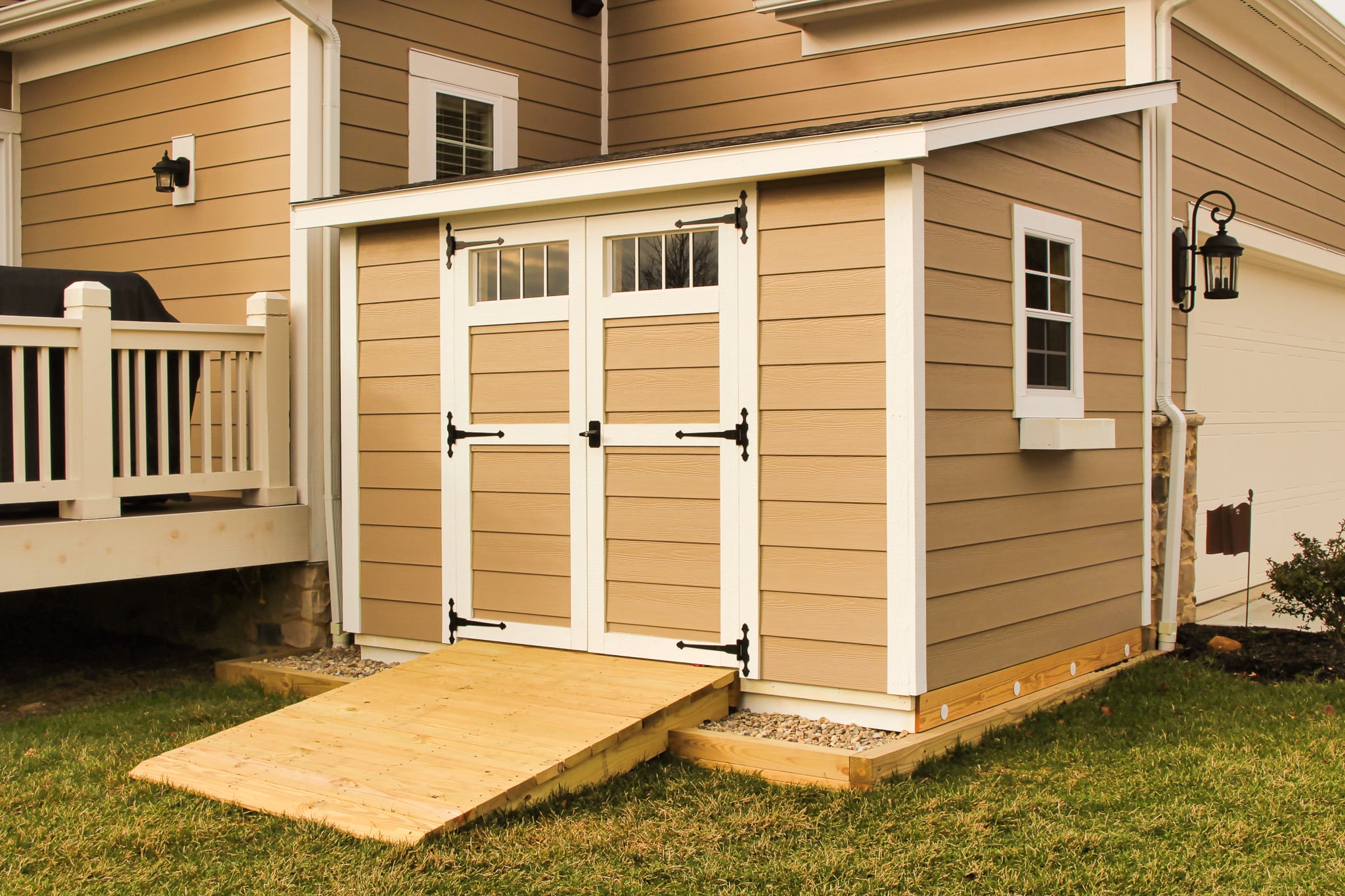 One of our Custom Sheds in Upper Arlington OH - Beige siding with white trimmed double doors and side window with white window box under sloped dark roof