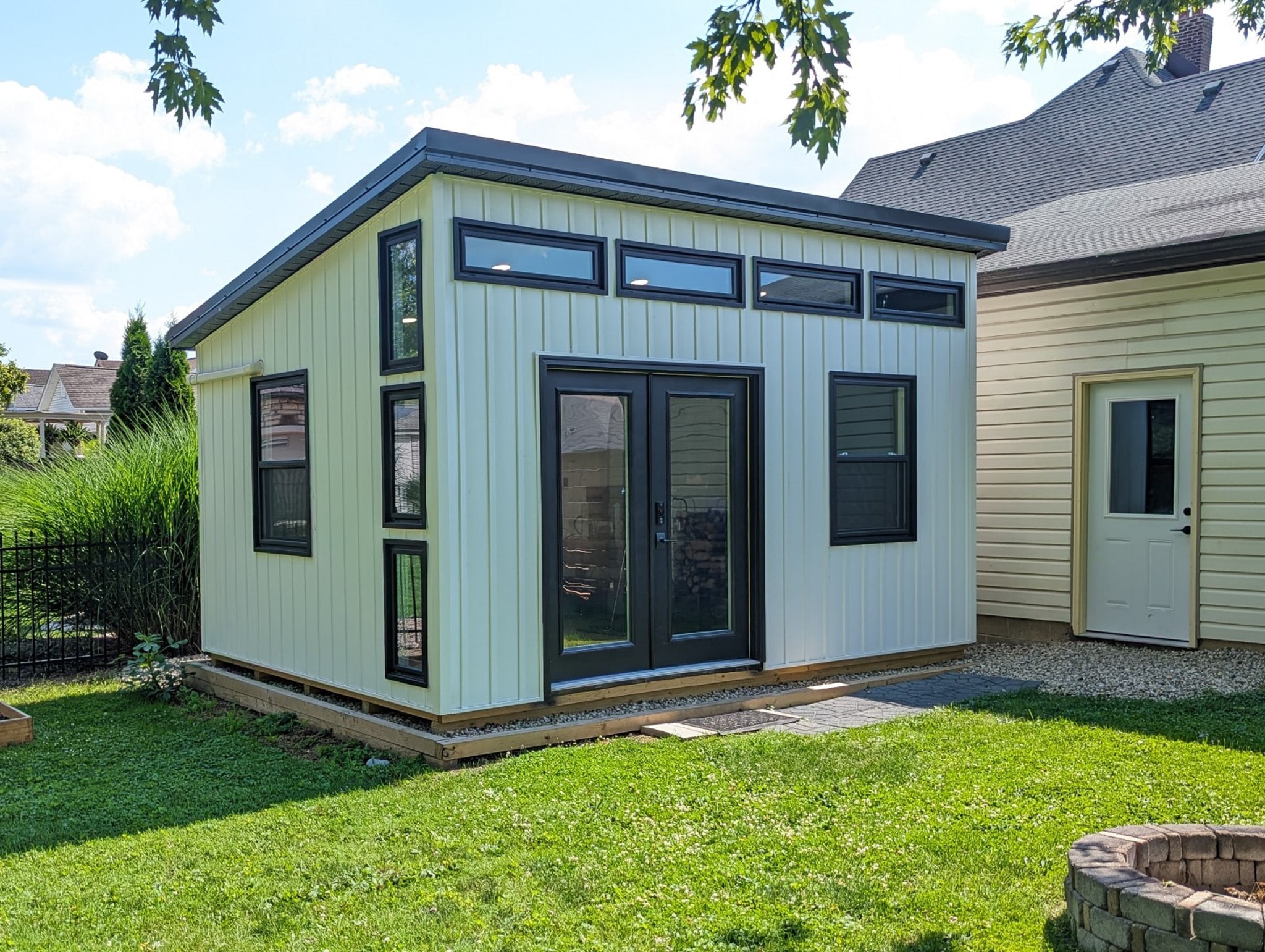 Modern studio shed with cream siding and large black-framed windows.