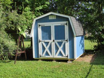 One of our mini Barn Sheds for sale in Dublin OH - Blue with white trimmed double doors and dark gray roof - on grassy yard under trees