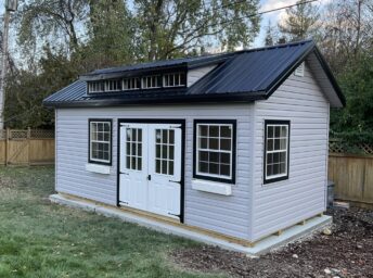 One of our cottage sheds for sale in Dublin OH - Gray siding with black and white trimmed double doors and windows - black roof with glass panes