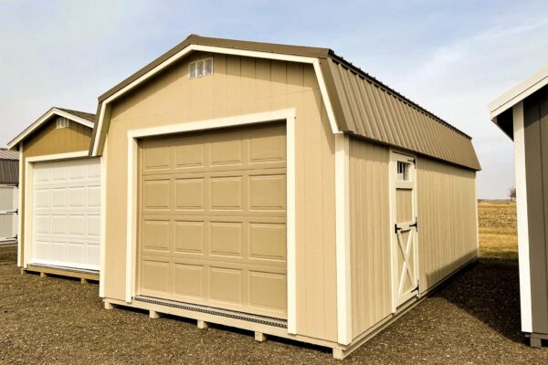 A beige Highwall garage shed with a large roll-up door and a side entry door, often seen in our quality sheds in Blacklick Estates, placed on a gravel surface under a cloudy sky.