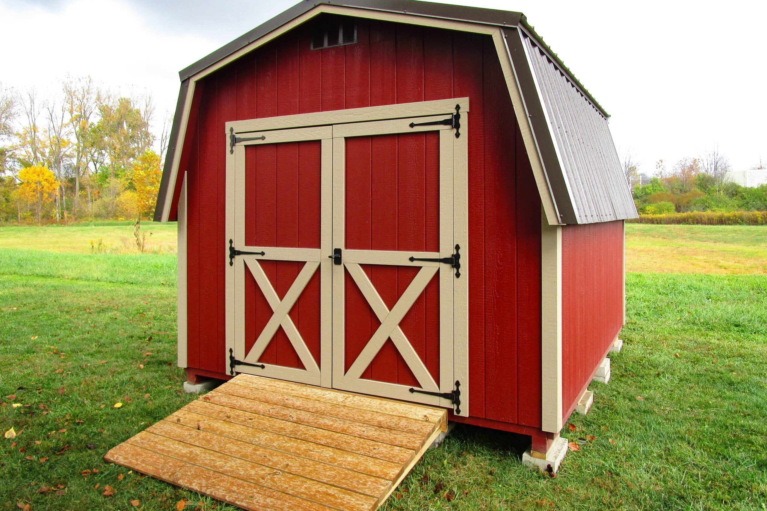 One of our red and beige Classic storage sheds for sale in Worthington OH - Red siding with beige trimmed double doors and brown roof - set in green yard with wooden ramp